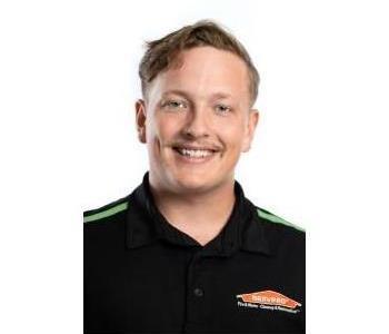 male employee smiling in front of green wall with orange servpro house